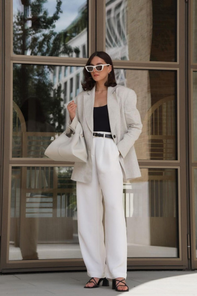 The brunette girl is dressed in old money style. She is wearing an oversize cream blazer, white women's trausers, black top and black pumps.