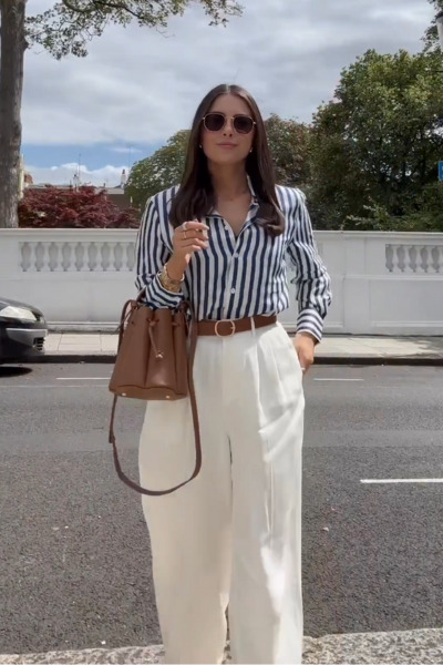 A woman dressed in old money style. She is wearing a classic striped shirt, white pants with a light brown belt and bag.